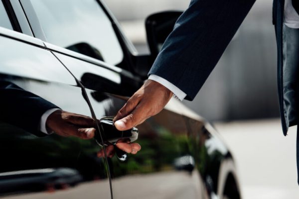 cropped view of african american businessman in suit opening car door at sunny day